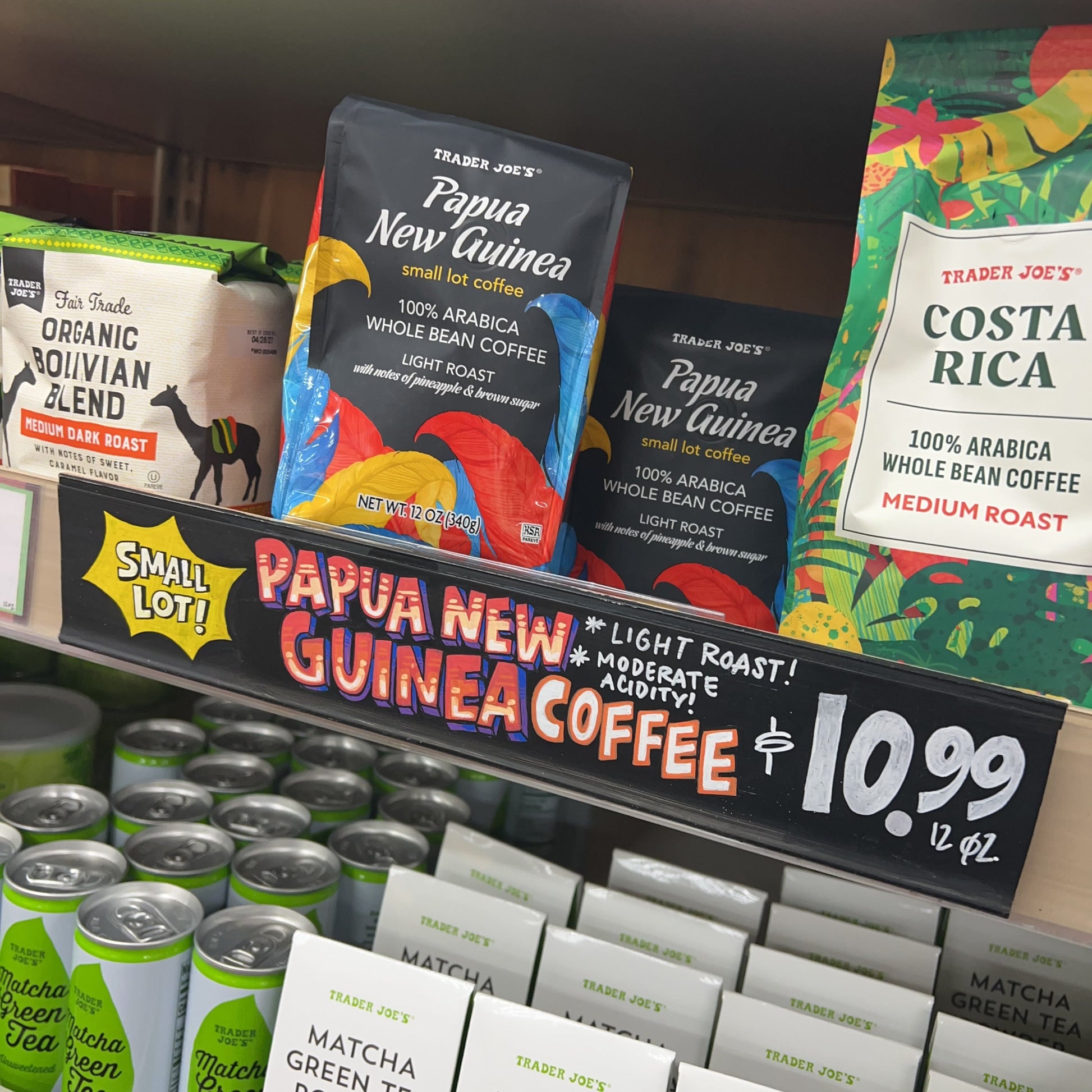 Trader Joe's Papua New Guinea Small Lot Coffee — in-store shelf display with handwritten sign: Small Lot! Papua New Guinea Coffee * Light Roast! * Moderate Acidity! $10.99 / 12 oz. Also visible: Trader Joe's Costa Rica Medium Roast and Organic Bolivian Blend Medium Dark Roast on same shelf