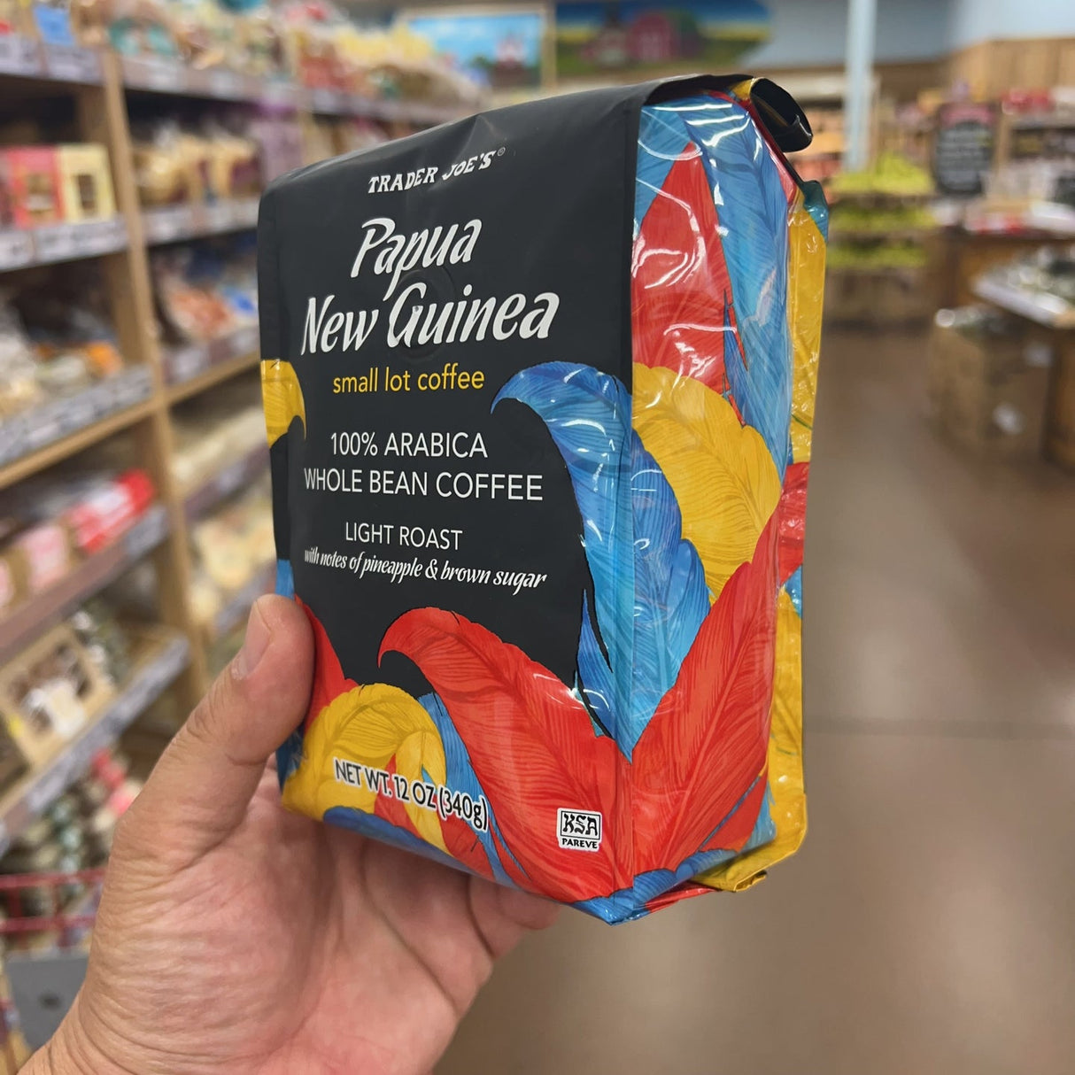 Trader Joe's Papua New Guinea Small Lot Coffee — front of bag, 100% Arabica Whole Bean Coffee, Light Roast, with notes of pineapple & brown sugar, net wt 12 oz (340g), Kosher Pareve (KSA), colorful tropical bird feather design on black bag